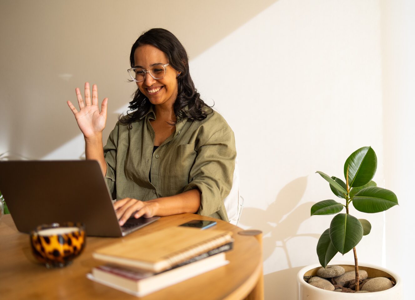 Smiling woman sits at her laptop and waves to greet her online coach