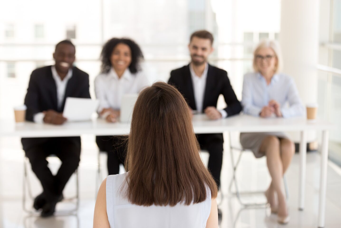 A woman sits in front of a board of smiling directors, worried about her first impressions