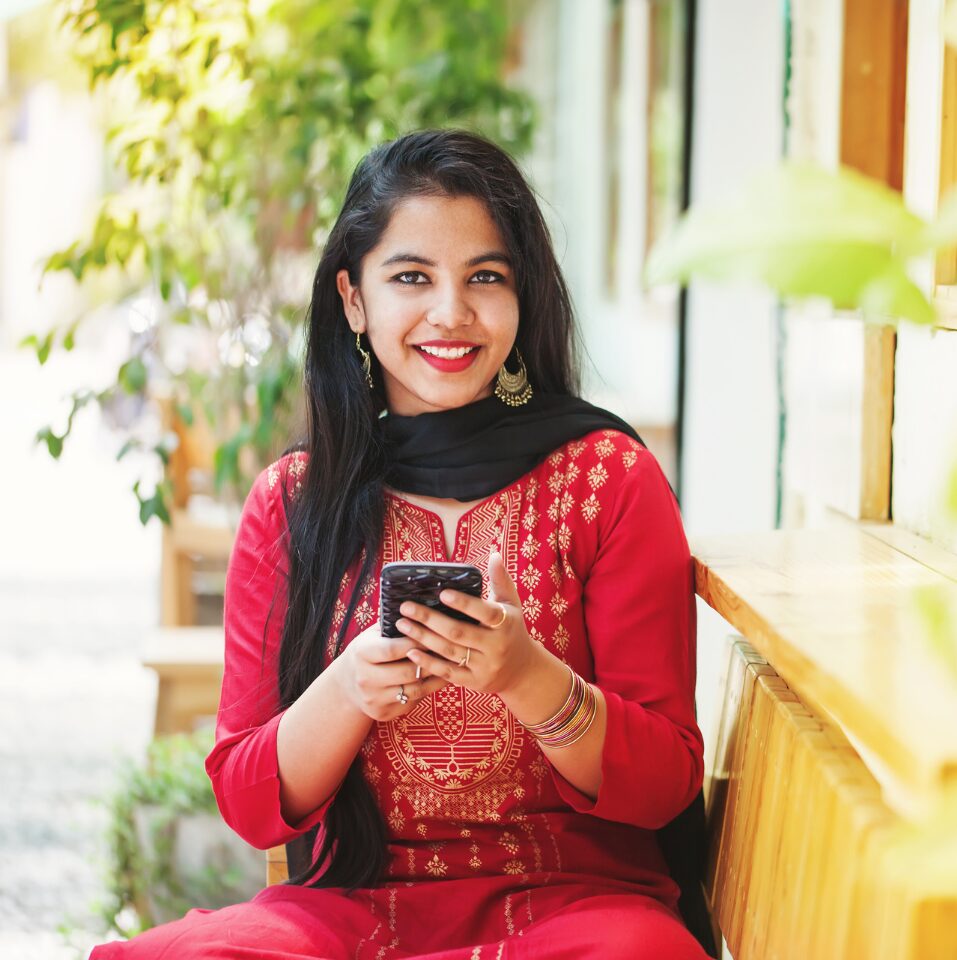 An Indian woman in traditional attire scrolls through content on her phone.