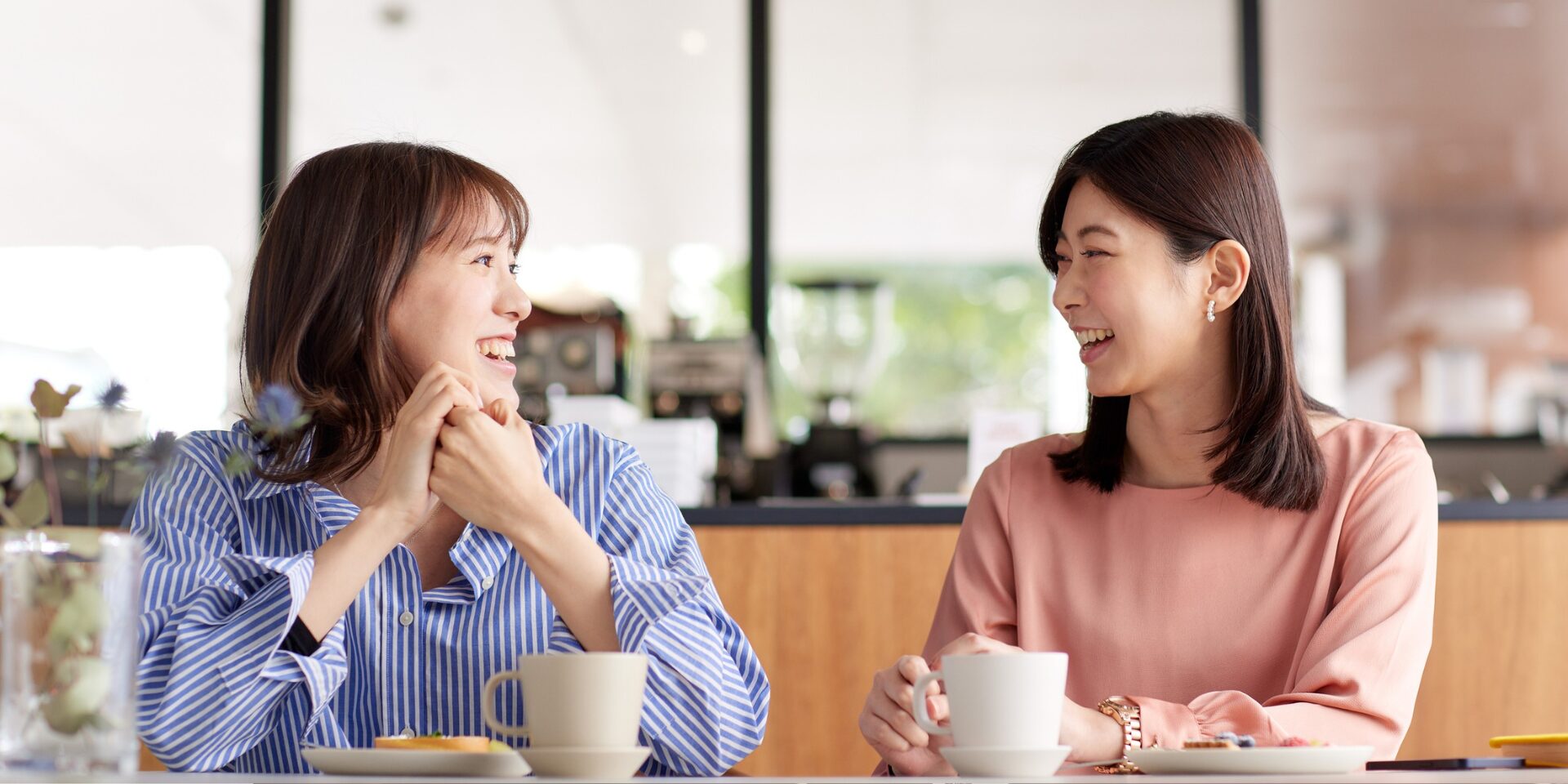 Two East Asian women have an enjoyable chat at a coffee shop.
