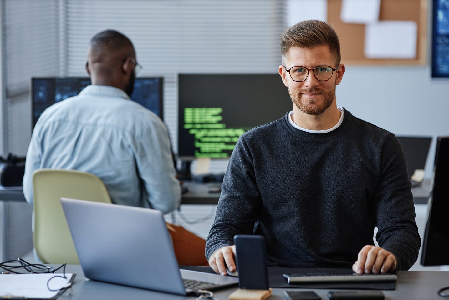 Two software engineers are shown. One is busy working and the other is looking up into the camera.
