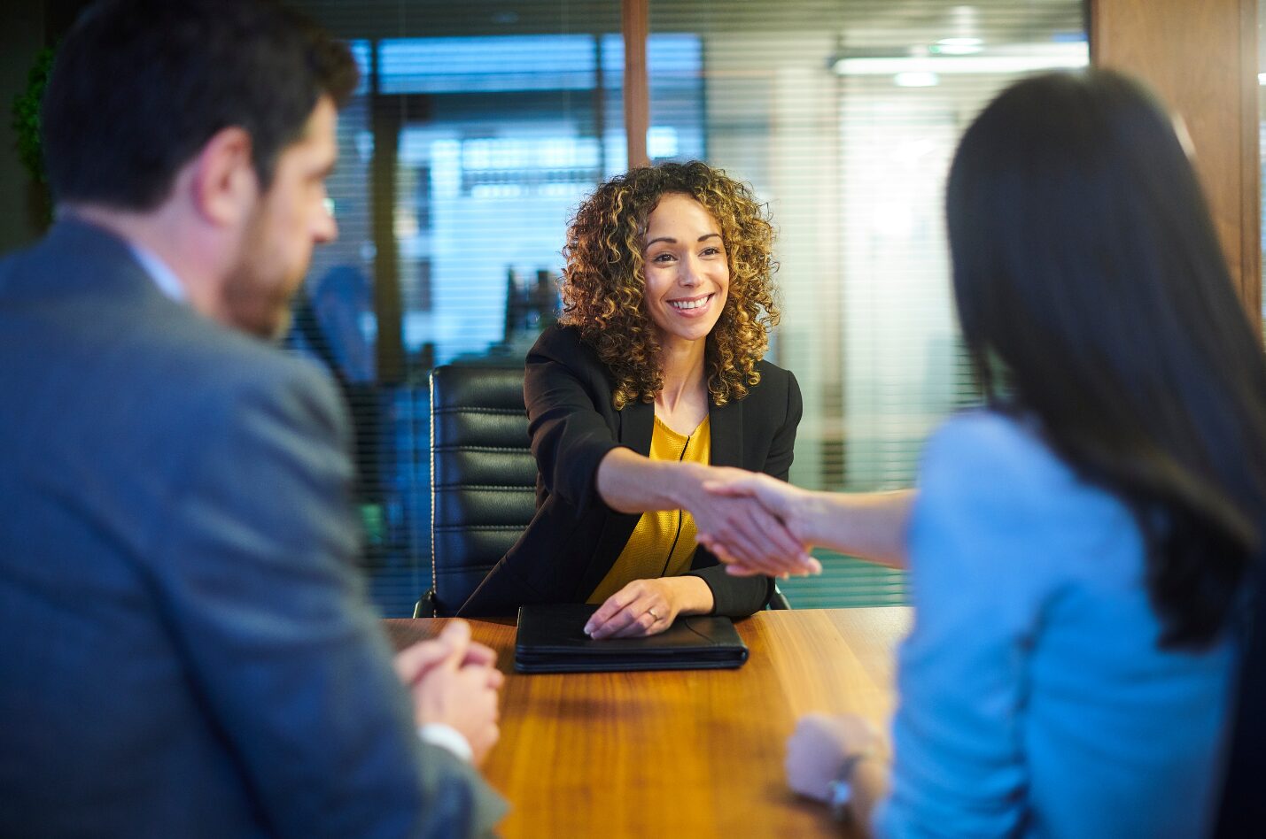 A woman smiles warmly and shakes her interviewer's hand, making a good first impression.