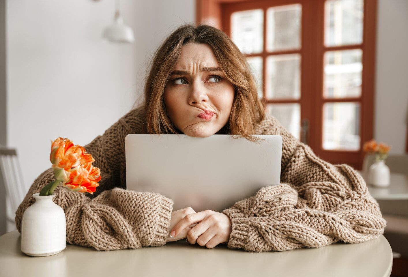 A woman leans over her computer with an uncertain, inquisitive expression.